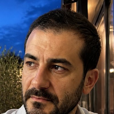 Kerem Demir, a bearded man with dark hair in a light grey shirt